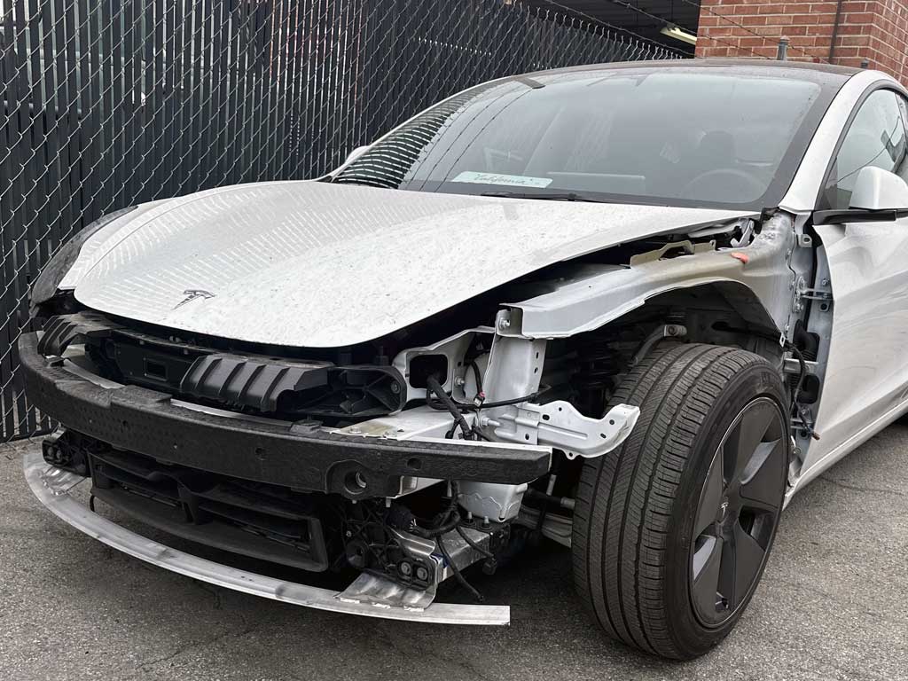 A silver car with its rear bumper missing, exposing internal components and mounting points. The vehicle appears stationary in a workshop setting, highlighting the need for bumper replacement and bodywork repair.